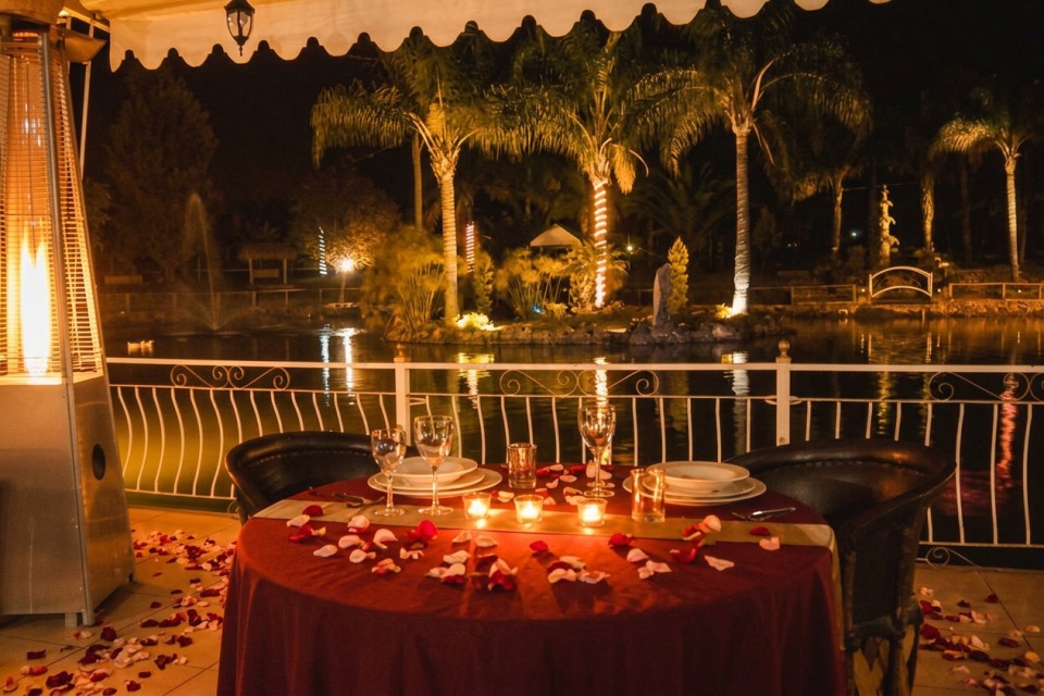 Mesa para dos con velas y pétalos junto al lago del restaurante, de noche
